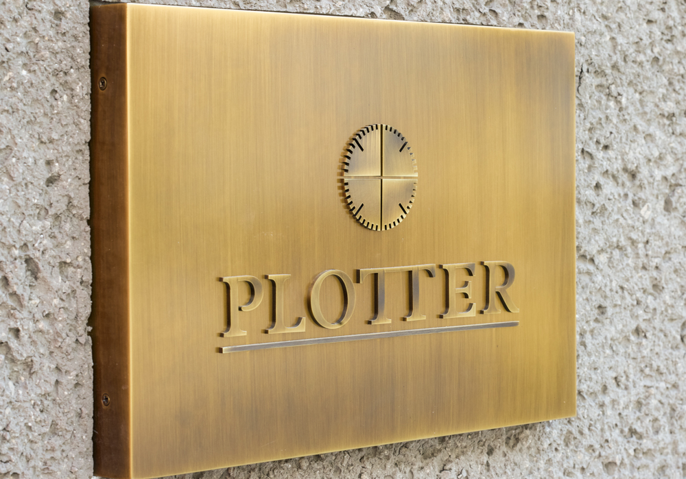 Brass plate on the exterior of a building with the PLOTTER logo.