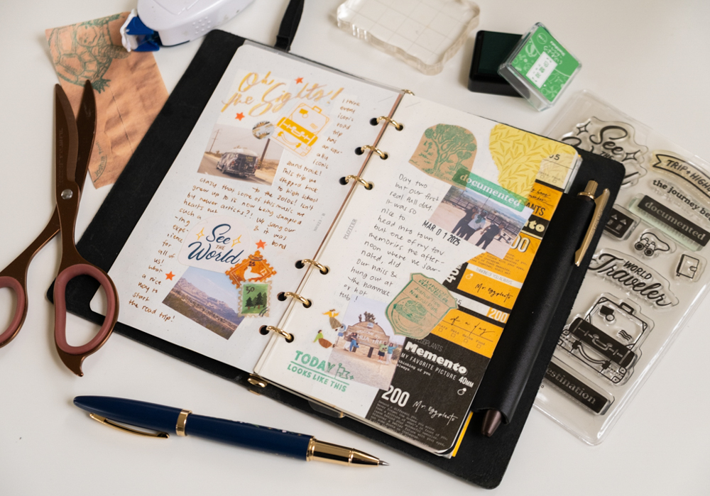 Open travel journal with colorful stickers, stamps, and handwritten notes. Scissors, pen, and stamps are scattered on a light surface, conveying creativity.
