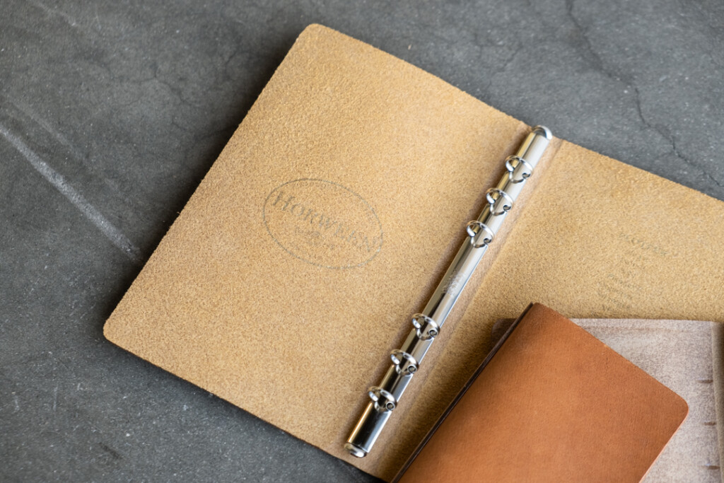 Three PLOTTER Leather Binders in Horween Predator Leather in Narrow Size, Bible Size and Mini 5 Size. All three binders are resting on concrete floor. The Bible Size PLOTTER is open to reveal the Horween logo on the left side of the Leather Binder.