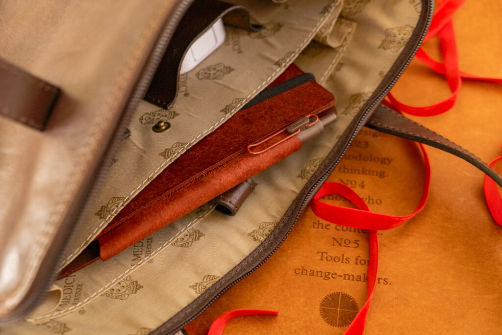 A red brown PLOTTER Leather Binder is inside a pocket in a leather shoulder bag.