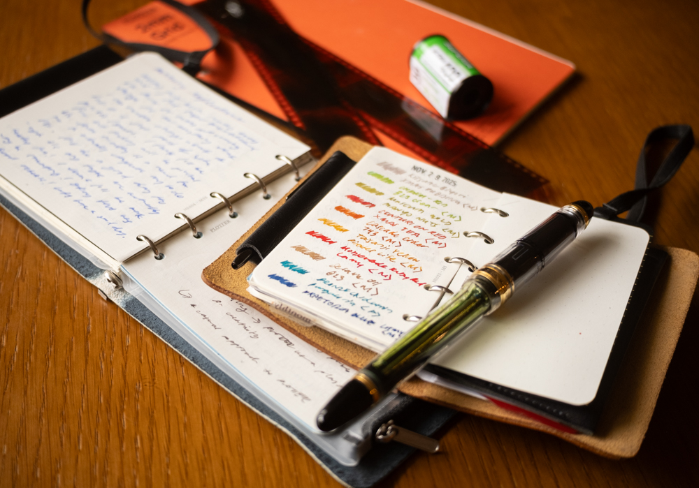 Various PLOTTER Leather Binders open on a wooden table, with other supplies nearby like a fountain pen, film, and refill memo pads.