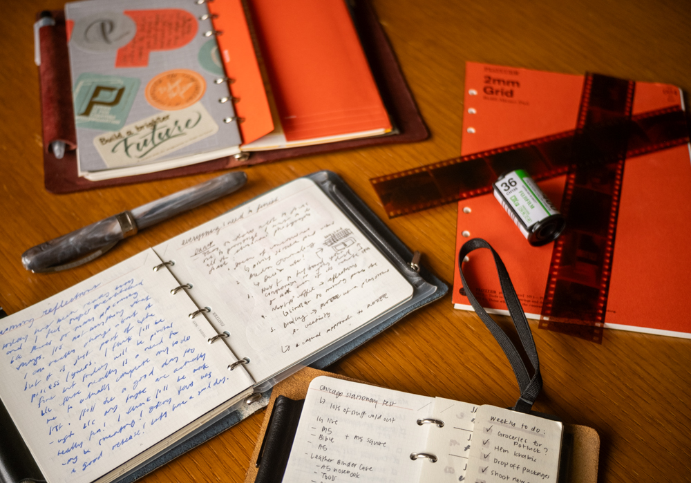 Various PLOTTER Leather Binders open on a wooden table, with other supplies nearby like a pen, film and a refill memo pads.