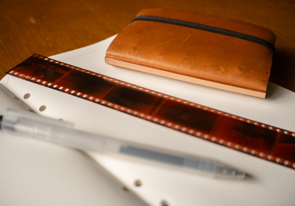 A refill memo pad open with a strip of developed film, a pen and a small Mini 5 Size PLOTTER Leather binder on the memo pad.