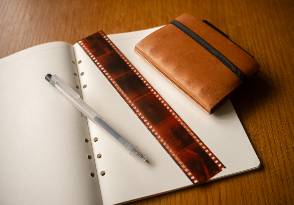 A refill memo pad open with a strip of developed film, a pen and a small Mini 5 Size PLOTTER Leather binder on the memo pad.
