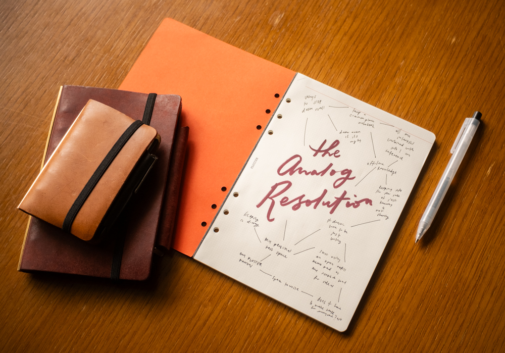 "The Analog Resolution" is handwritten on a memo pad beside PLOTTER Leather Binders and a brush marker.