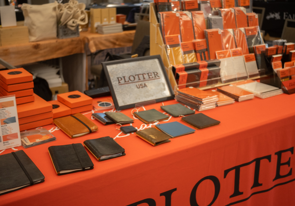 PLOTTER USA table filled with PLOTTER items, leather binders, and stationery at the California Pen Show.