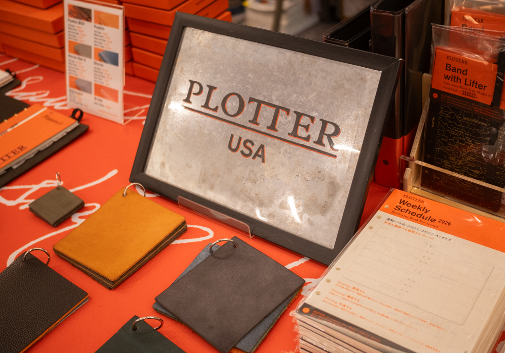 PLOTTER USA table filled with PLOTTER items, leather binders, and a hand-painted sign at the California Pen Show.