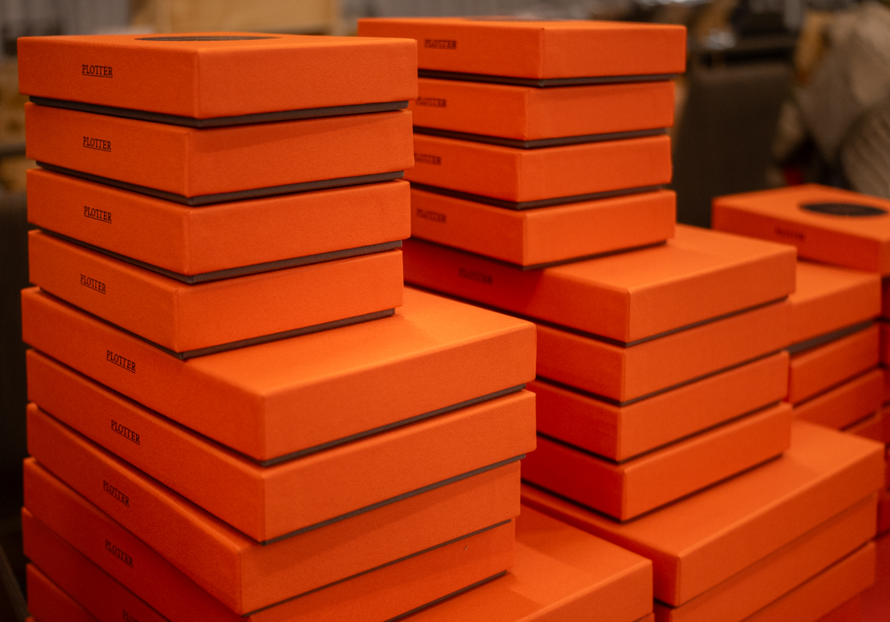 Stacks of orange PLOTTER boxes filled with Leather Binders in various sizes.