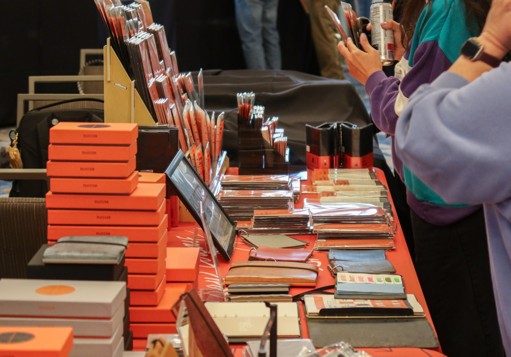 A side view of the PLOTTER USA table filled with PLOTTER items, leather binders, and stationery at the California Pen Show.