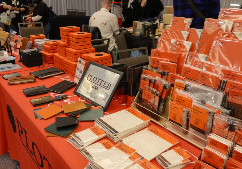 PLOTTER USA table filled with PLOTTER items, refill memo pads, leather binders, and stationery at the California Pen Show.