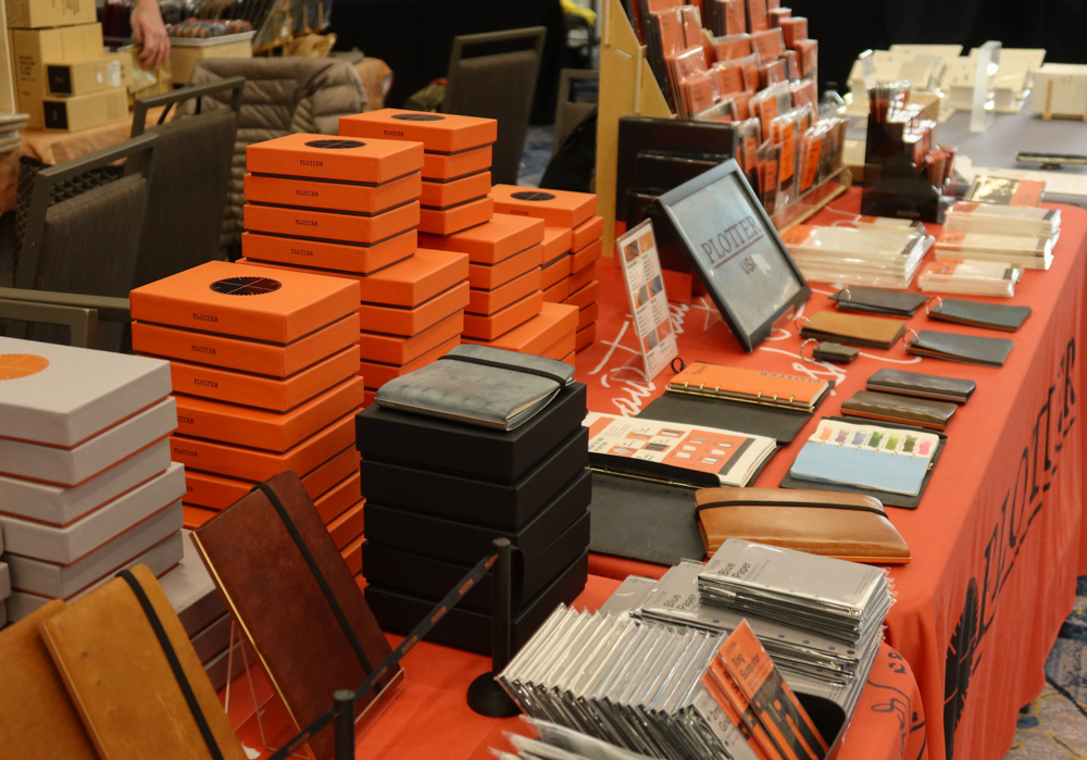 PLOTTER USA table filled with PLOTTER items, leather binders, and stationery at the California Pen Show.