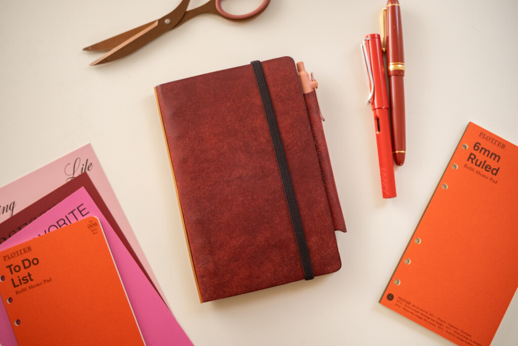 A Red Brown PLOTTER Leather Binder in Bible Size, beside PLOTTER Refill Memo Pads and red fountain pens.