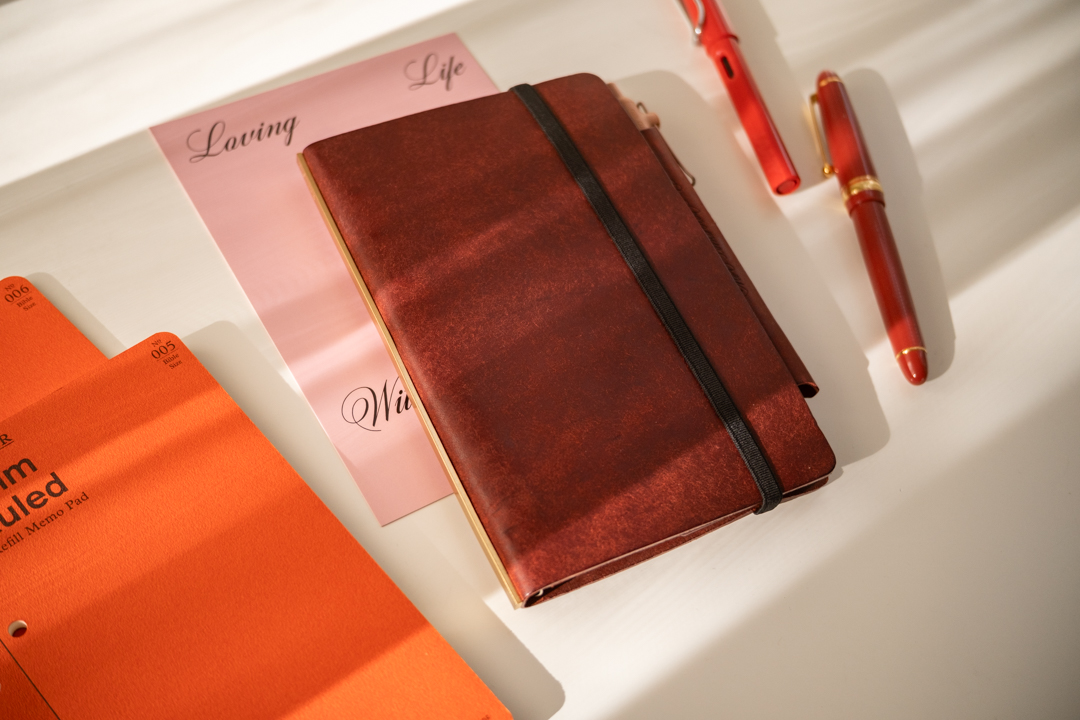 A Red Brown PLOTTER Leather Binder in Bible Size, beside PLOTTER Refill Memo Pads and red fountain pens.