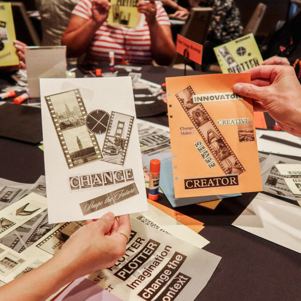 Two people are showing off their finished collages at a collaging station on a round table filled with paper supplies and glue.