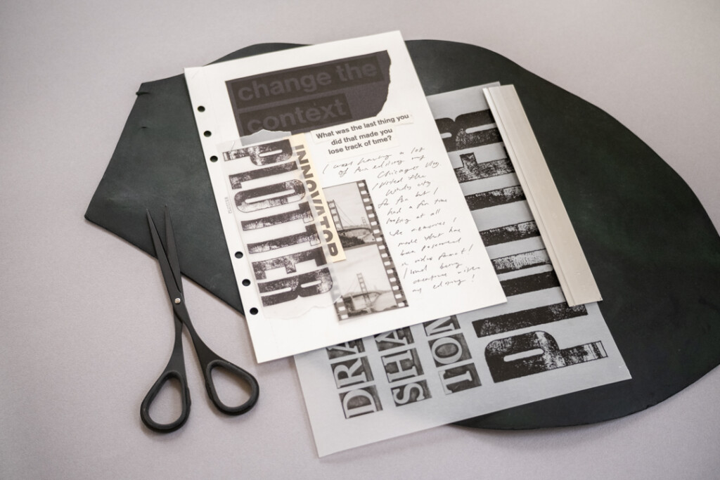 A collage on white paper with black and white graphics and pictures which is on top of a leather mat and a grey table.