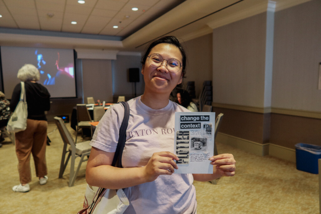 A person showing off their finished collages in an event space filled with tables.
