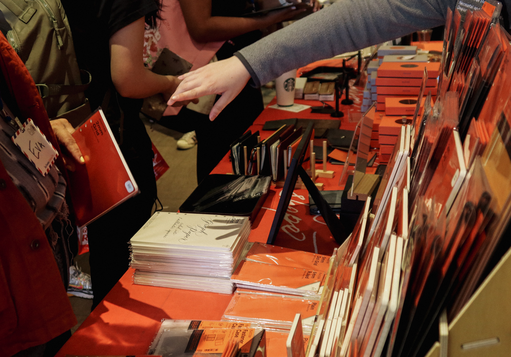 A person shopping at the PLOTTER USA table filled with PLOTTER items, leather binders, and stationery at the San Francisco Stationery Fest.
