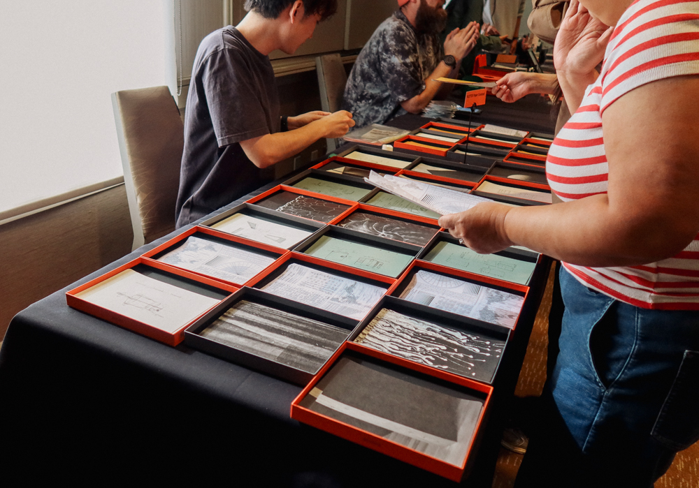 A person choosing different papers from a table filled with different collage materials, papers, and ephemera.