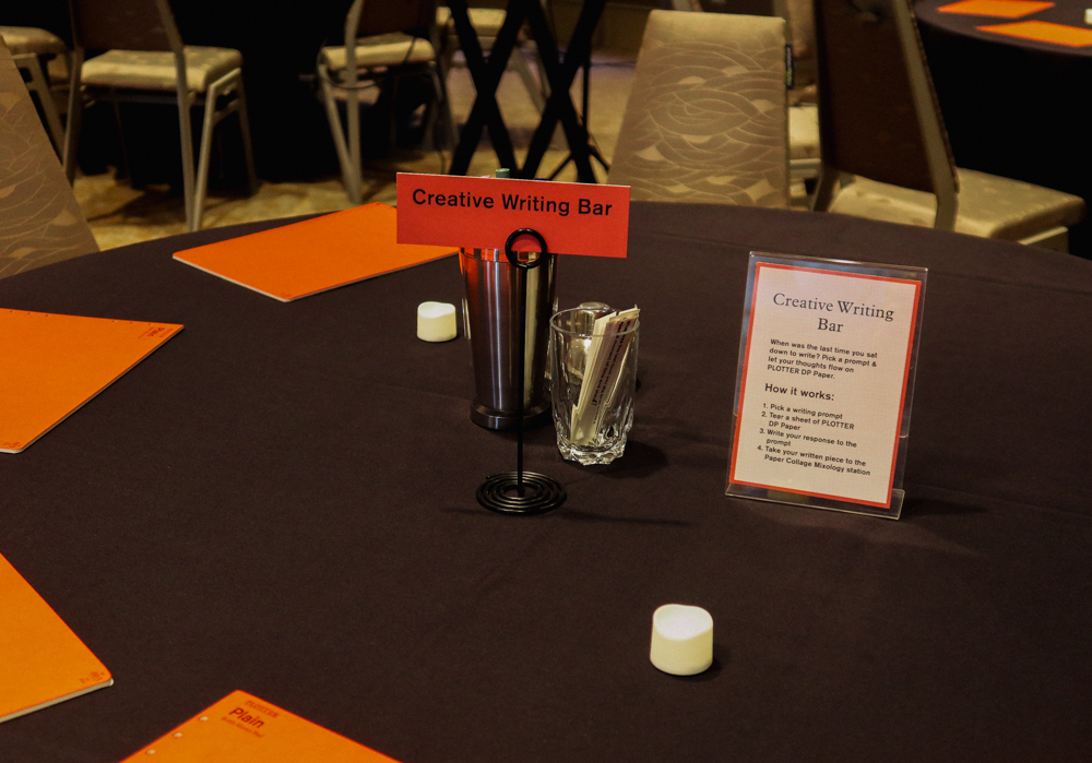 A round table with a black tablecloth with different PLOTTER refill memo pads and writing utensils on it.