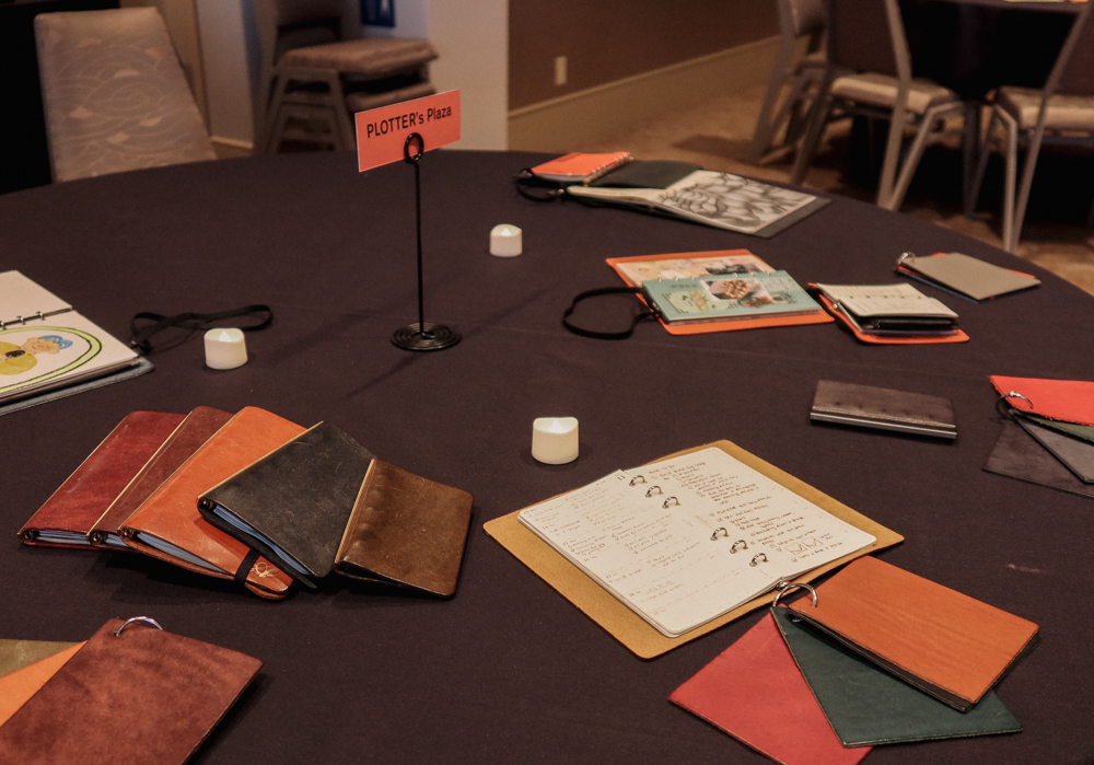A round table with a black tablecloth with different PLOTTER Leather Binders and accessories on it.