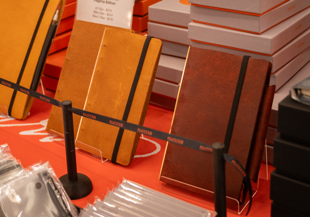 Red leather binder beside beige leather binders on the PLOTTER USA table.
