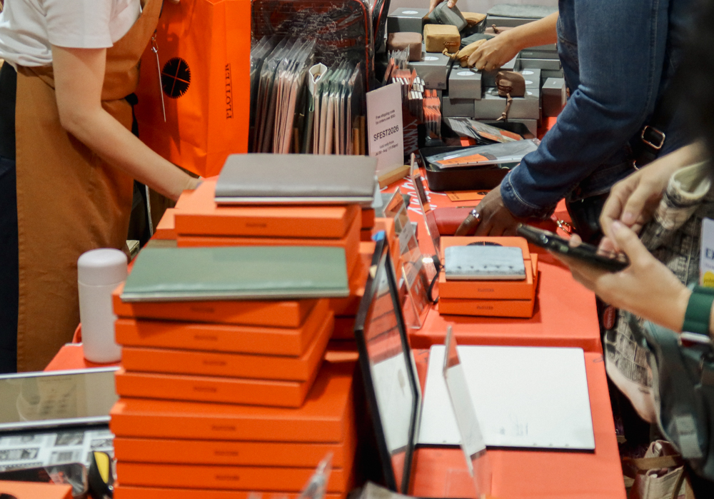 A PLOTTER team member showing a leather binder to a customer at the PLOTTER USA table at Stationery Fest 2026.