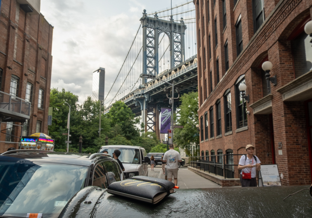 A PLOTTER mini 5 leather binder resting on a mailbox with the Manhattan Bridge in the background.