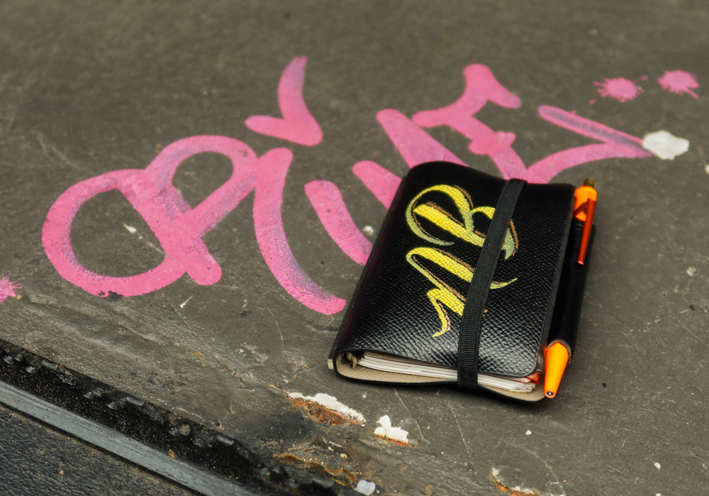 A PLOTTER mini 5 leather binder resting on some graffiti on the road.