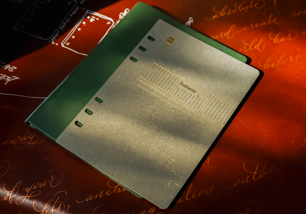 The Limited Edition Subway paper divider for A5 size PLOTTER on top of a green leather binder.