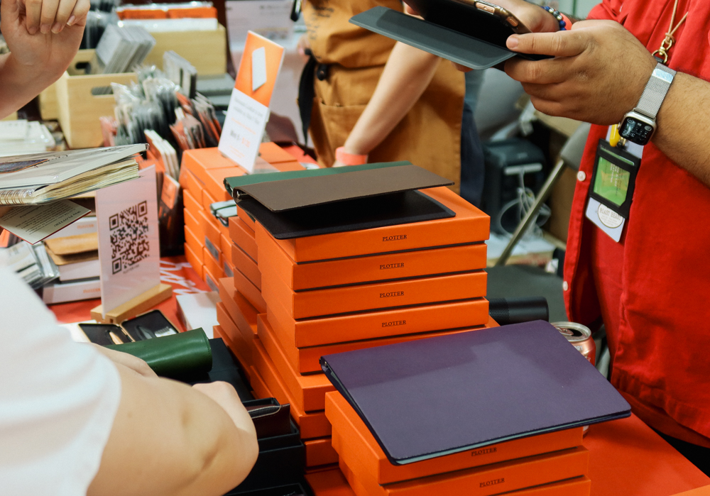 A PLOTTER team member showing a leather binder to a customer at the PLOTTER USA table at Stationery Fest 2026.